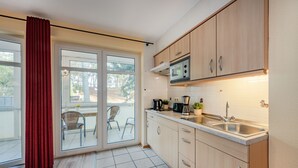 Una cocina moderna con microondas, fregadero y armarios. Hay una puerta corrediza de vidrio que da a un patio con sillas.