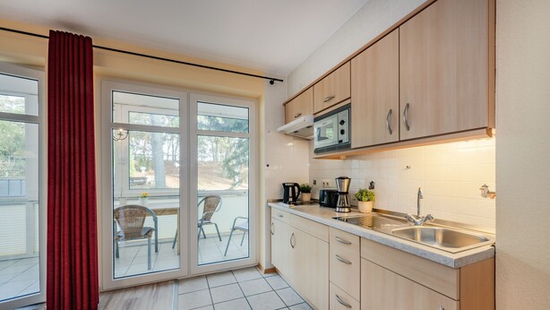 Una cocina moderna con microondas, fregadero y armarios. Hay una puerta corrediza de vidrio que da a un patio con sillas.