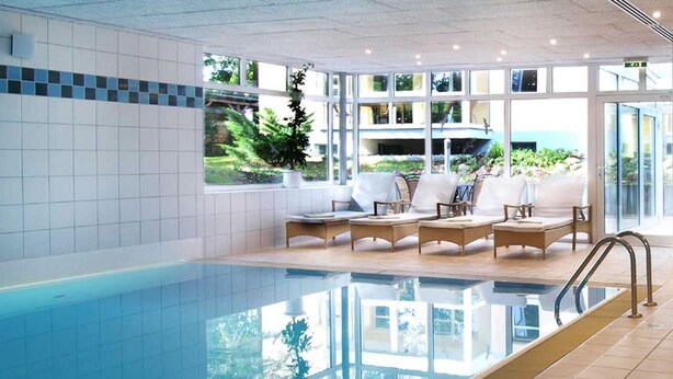 Zona de piscina con vista a un edificio y vegetación.