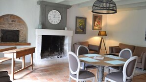 A cozy living room with a fireplace, a dining table with chairs, a sofa, and a hanging light fixture.