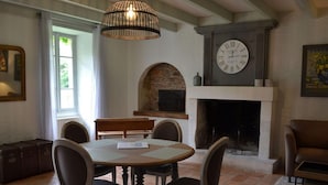 A dining area with a round table, four chairs, a fireplace, and a large wall clock.