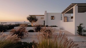 A modern white building with a flat roof, surrounded by gravel pathways and various shrubs. - Villa Dia, Mikri Vigla, Panagia Parthena Beach (Naxos)