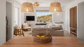 A modern living room with a wooden dining table, wicker lamps, a sofa, and a TV. - Villa Dia, Mikri Vigla, Panagia Parthena Beach (Naxos)