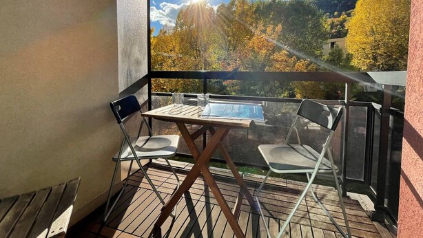 A balcony with a table and chairs, overlooking a scenic view of autumn trees and a clear sky.