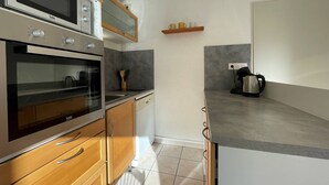 A modern kitchen with a built-in oven, microwave, and dishwasher. There is a coffee maker on the countertop and a wooden cabinet above the sink.