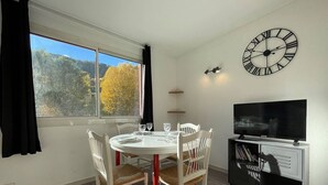 A dining area with a round table, white chairs, a TV, and a wall clock.