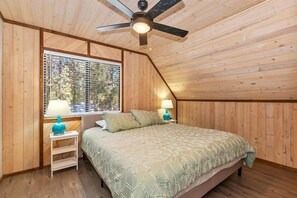 Une chambre avec un plafond en pente, un lit recouvert d’une couvre-lit à motifs, deux lampes de chevet et une fenêtre avec des stores.