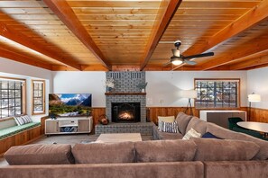 Ein gemütliches Wohnzimmer mit Kamin, Holzbalkendecke, Fernseher und einer Couch.