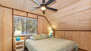 Ein Schlafzimmer mit einem Bett, zwei Nachttischen, einem Deckenventilator und einem Fenster mit Jalousien.