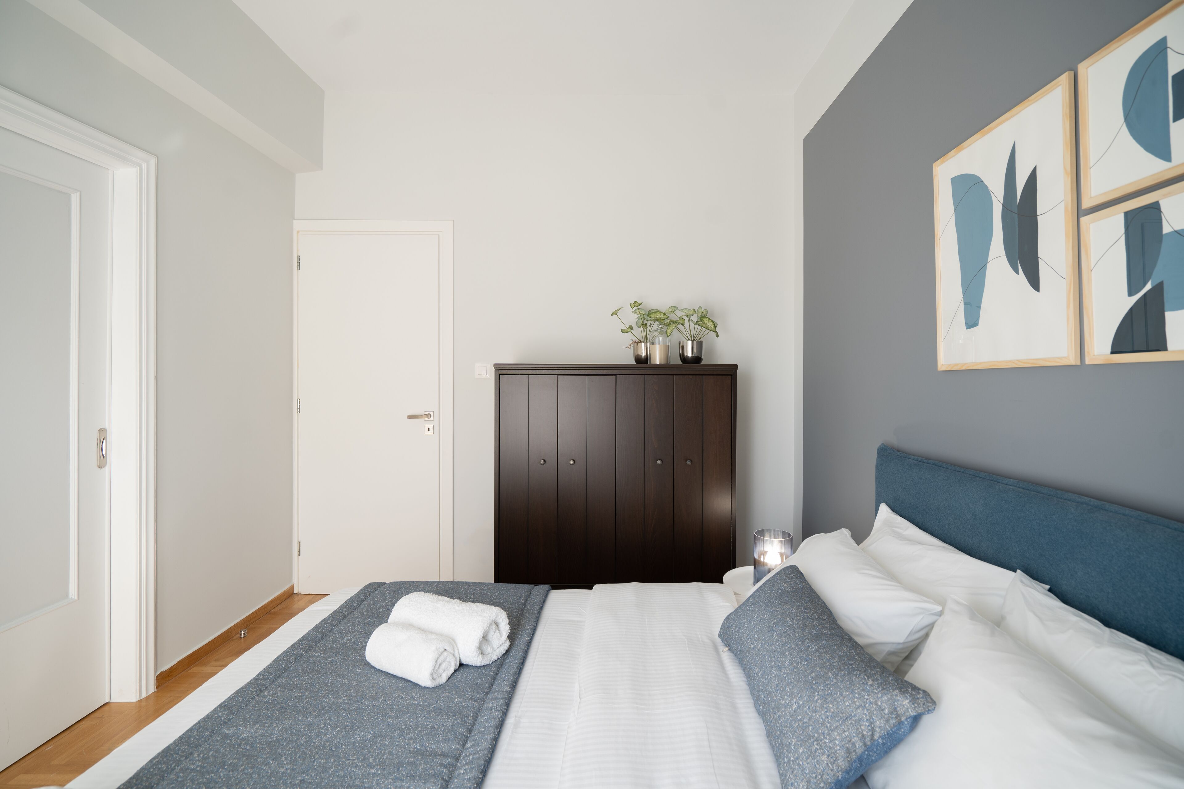 Une chambre à coucher avec un lit, une armoire et un mur décoré d’œuvres d’art abstraites.