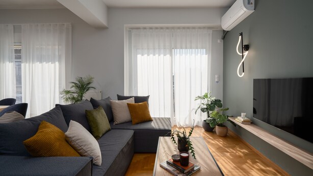 A modern living room with a sectional sofa, a coffee table with books and a plant, and a flat-screen TV mounted on the wall. - Deluxe 4 Bedrooms Apartment in Athens Center (Athens)