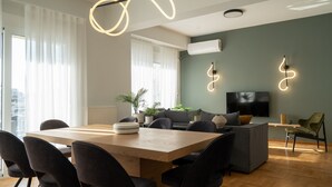 A modern living room with a wooden dining table, black chairs, a grey sofa, and a flat-screen TV mounted on the wall. - Deluxe 4 Bedrooms Apartment in Athens Center (Athens)