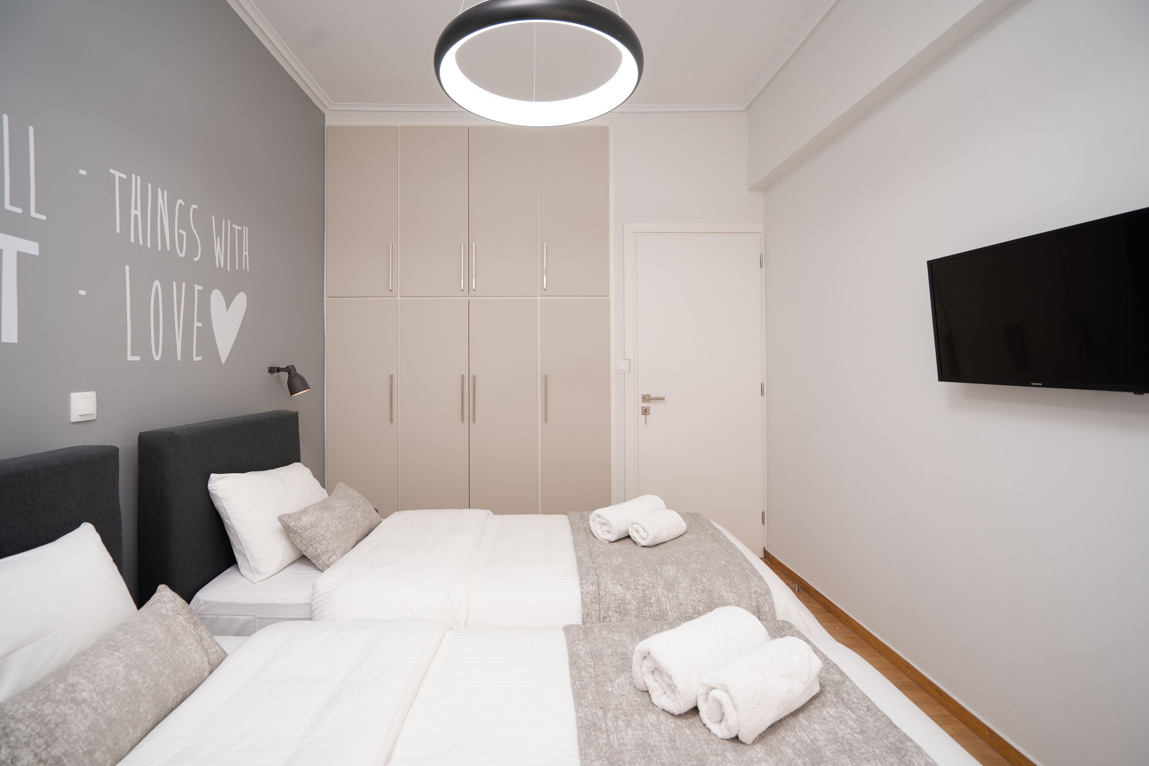 A bedroom with a bed, two nightstands, a wardrobe, a flat-screen TV, and a wall with a motivational quote.