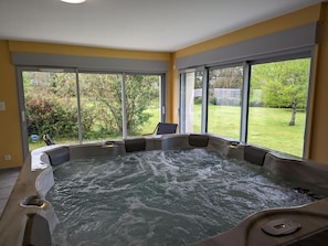 A hot tub with a view of a garden through large windows.