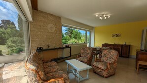 A living room with patterned sofas, a small table, and a view of greenery through large windows. - Comfortable house with private garden, internet, parking (Agris)