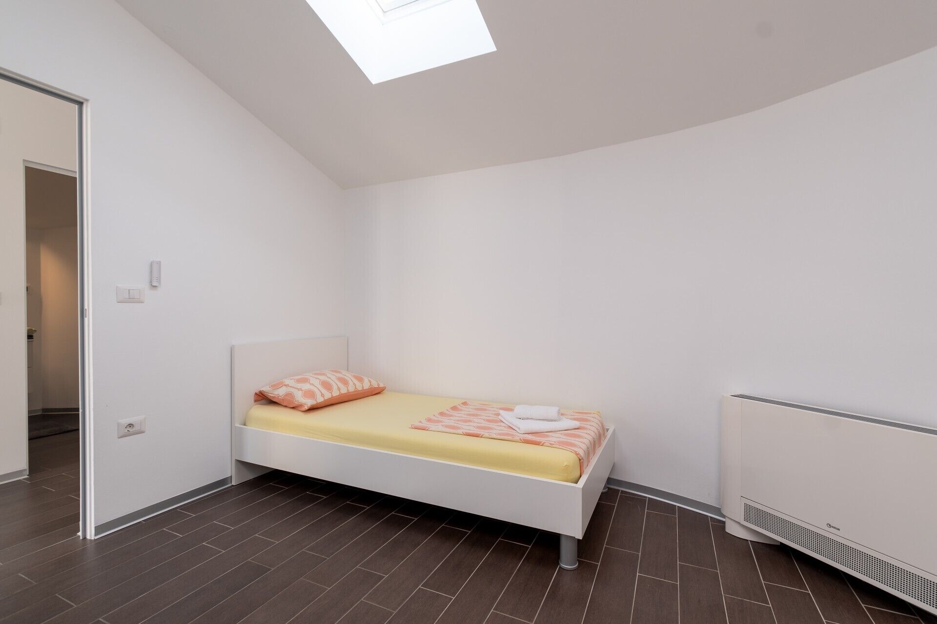 Une petite chambre à coucher moderne, avec un lit, un radiateur et une lucarne.
