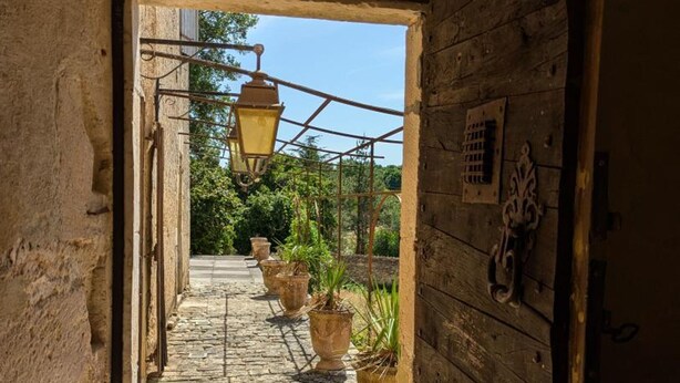 Un estrecho sendero de piedra que atraviesa un rústico edificio de madera, con plantas en macetas a lo largo del camino y un farol colgante.