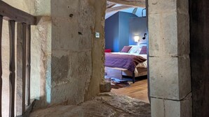 Una habitación rústica con vigas de madera a la vista, una cama con ropa de cama estampada y un ventanal pequeño.