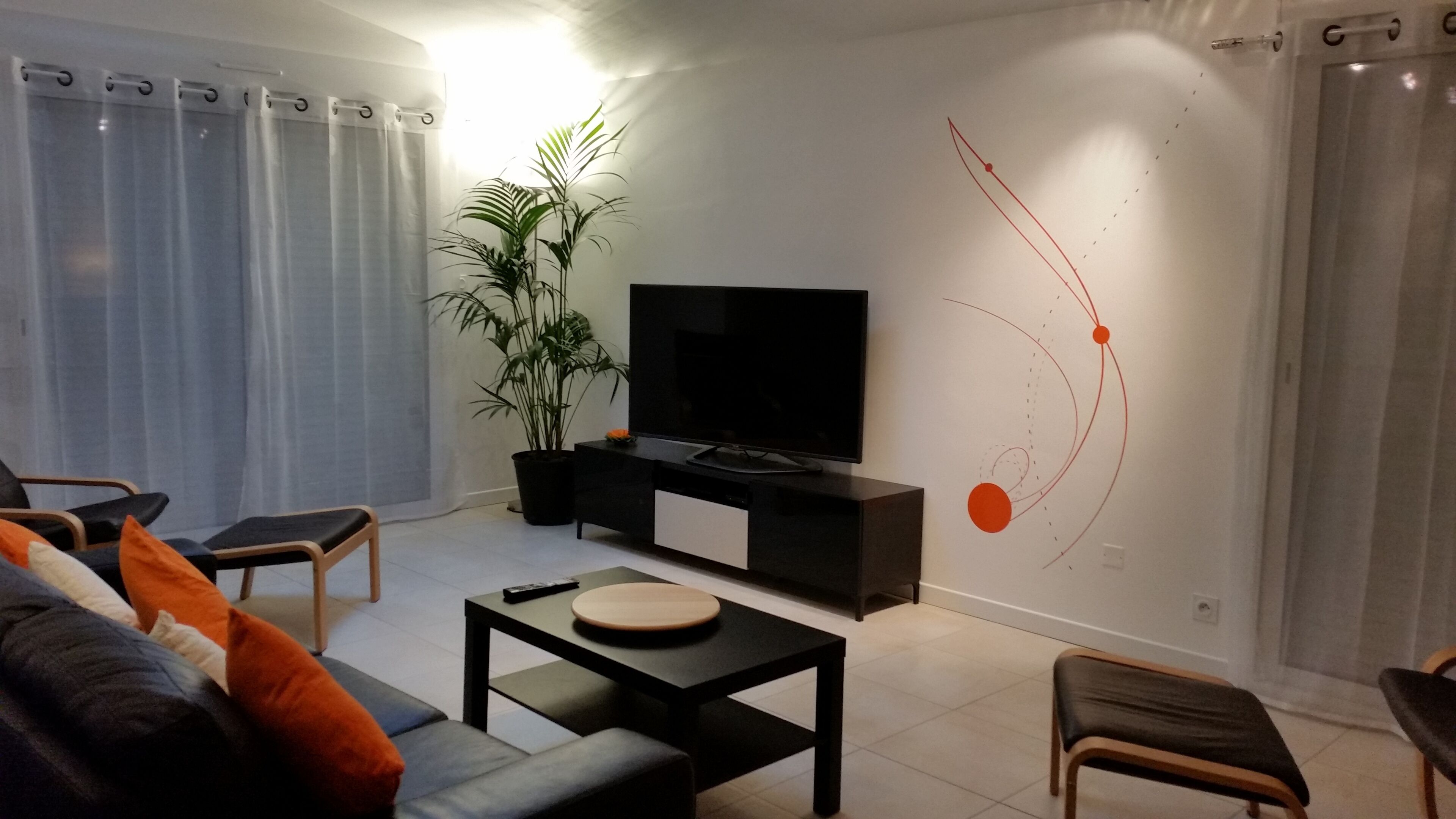 Un salon doté d’un téléviseur à écran plat, d’une plante en pot et d’un mur au décor sobre.