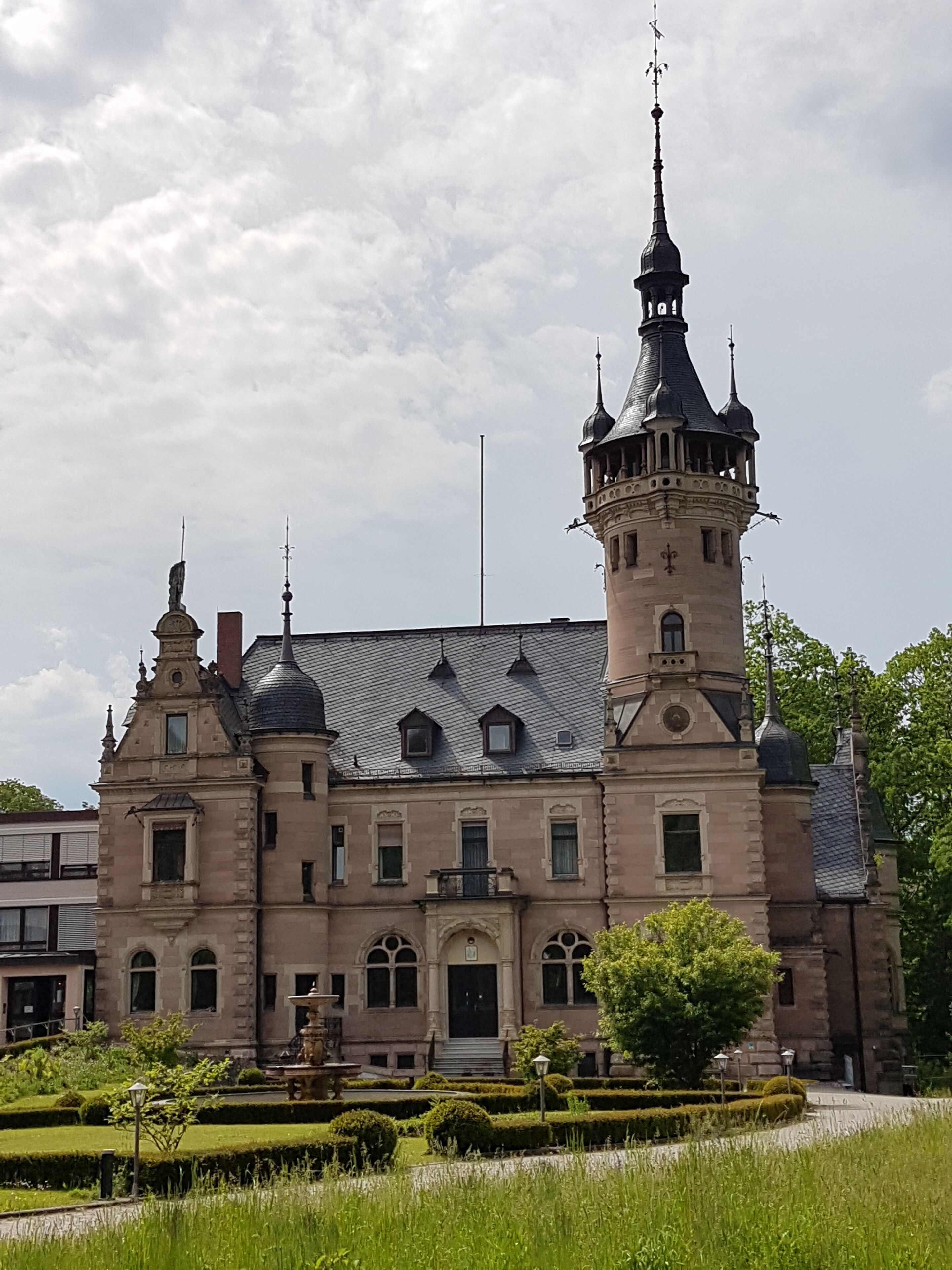 A historic building with a prominent tower, symmetrical windows, and a well-maintained garden.