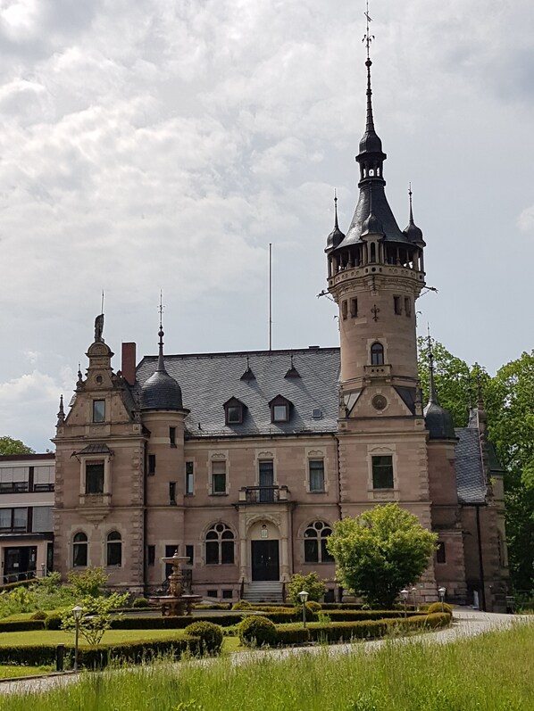 A historic building with a prominent tower, symmetrical windows, and a well-maintained garden.