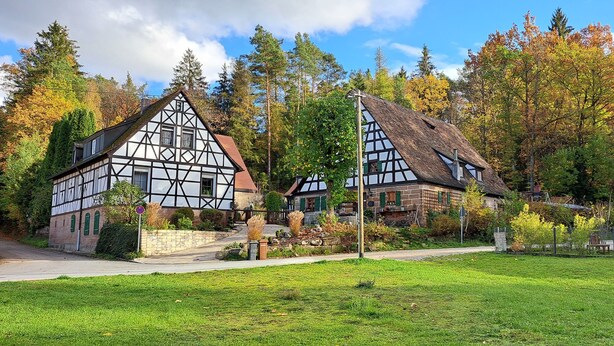 Une maison traditionnelle à colombages, dotée d’un toit en pente, entourée d’une pelouse bien entretenue et d’arbres touffus.