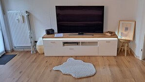 Un salon moderne doté d’un grand téléviseur à écran plat, d’un meuble de rangement blanc, d’une table basse en bois, d’un tableau encadré et d’un tapis à motifs animaliers originaux.