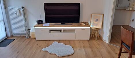 Un salon moderne doté d’un grand téléviseur à écran plat, d’un meuble de rangement blanc, d’une table basse en bois, d’un tableau encadré et d’un tapis à motifs animaliers originaux.