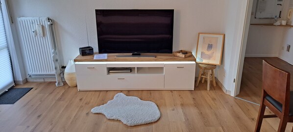 A modern living room with a large flat-screen TV, a white entertainment unit, a wooden coffee table, a framed picture, and a unique animal print rug. - Beautiful and cozy vacation apartment in the Schwarzachtal - NO MONTEURE- (Schwarzenbruck)