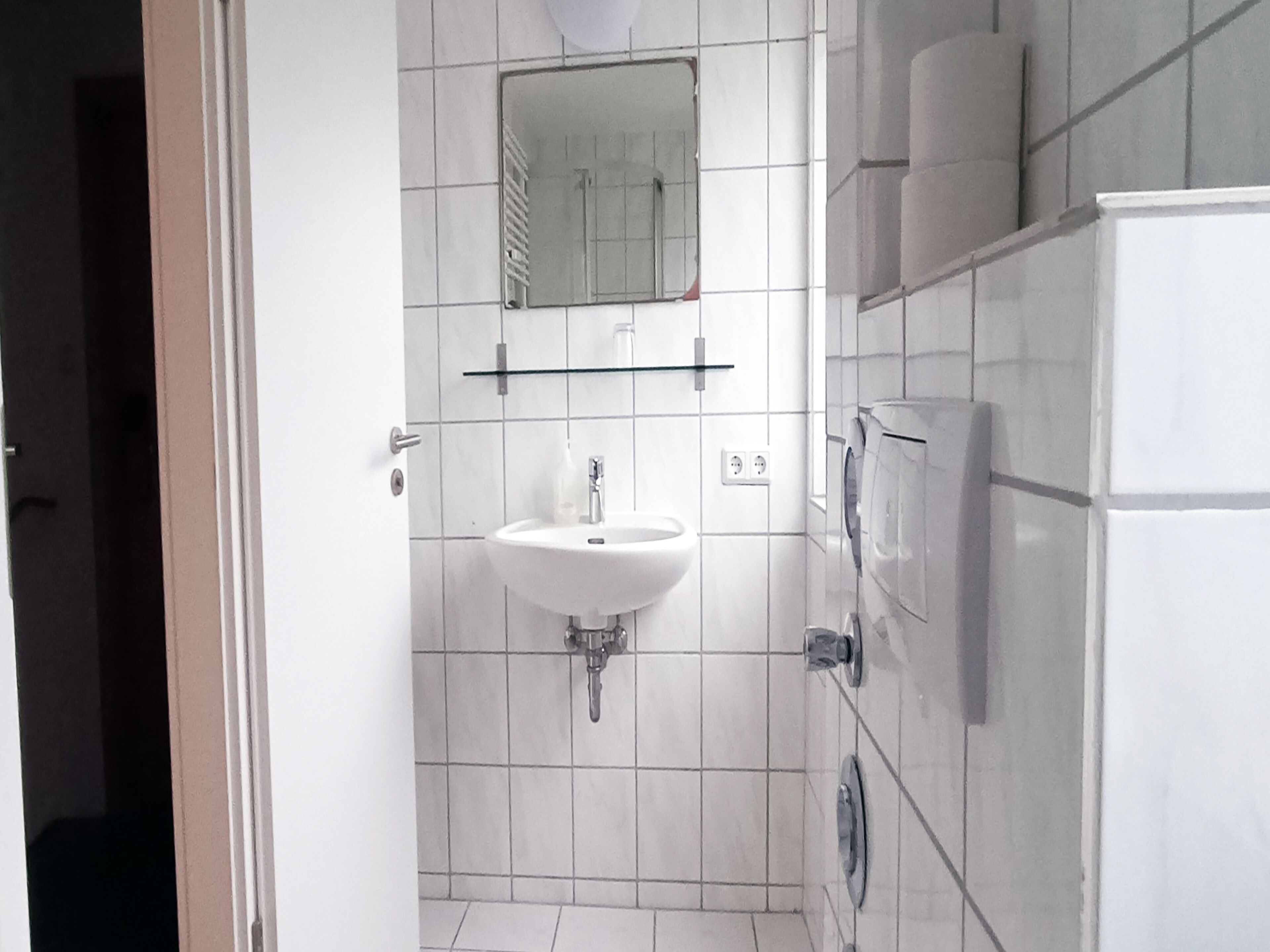 Et badeværelse med hvid vask, spejl og flisebeklædte vægge.