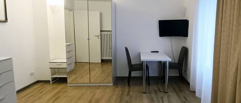 A hotel room with a bed, a desk, a chair, a TV, and a wardrobe.