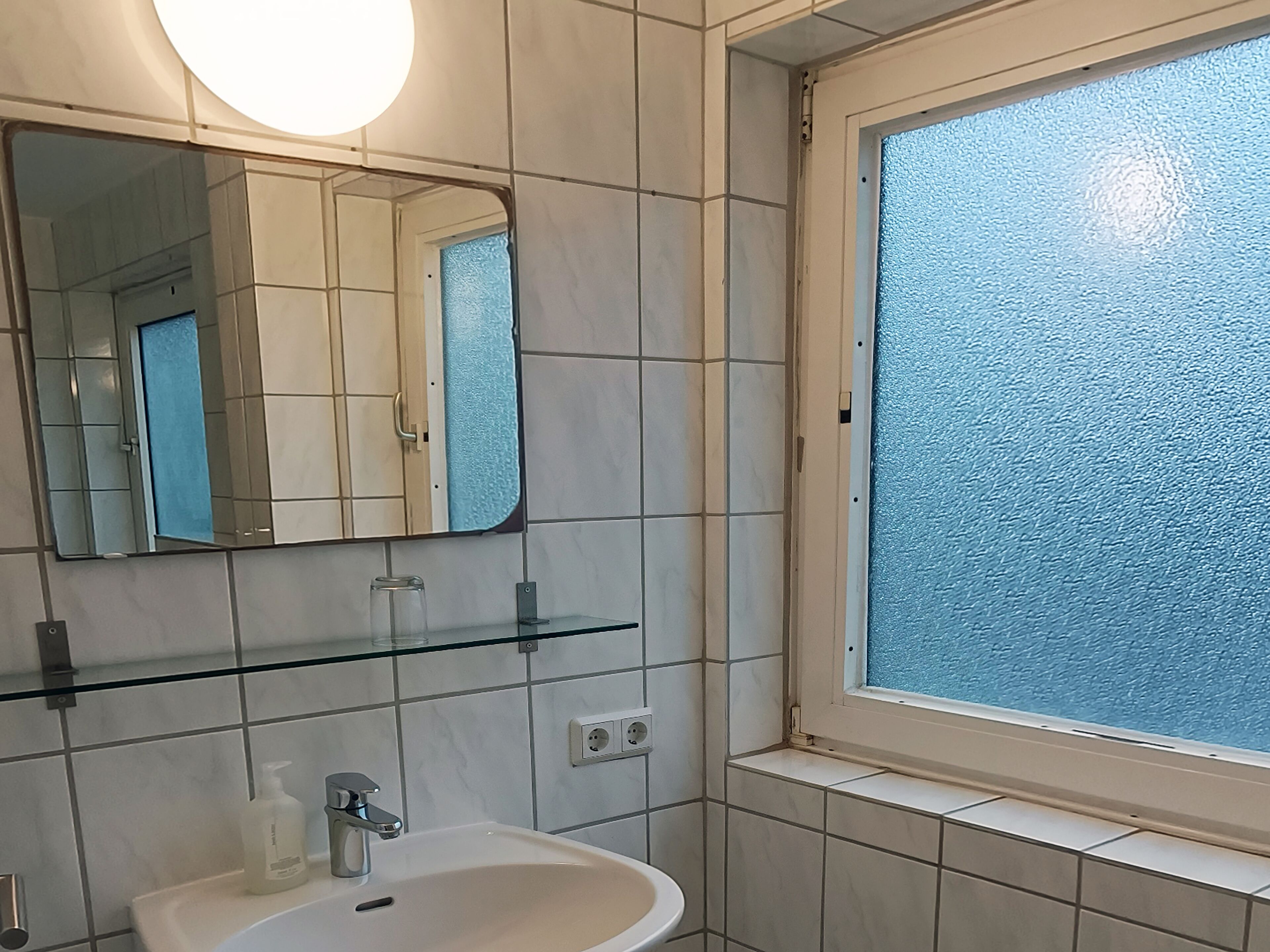 A bathroom with a white sink, a mirror, and a window with frosted glass.