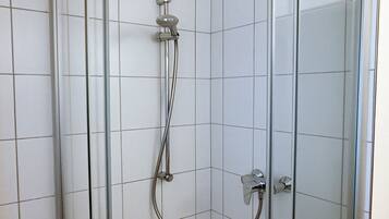 A glass-enclosed shower with a handheld showerhead and a flexible hose.