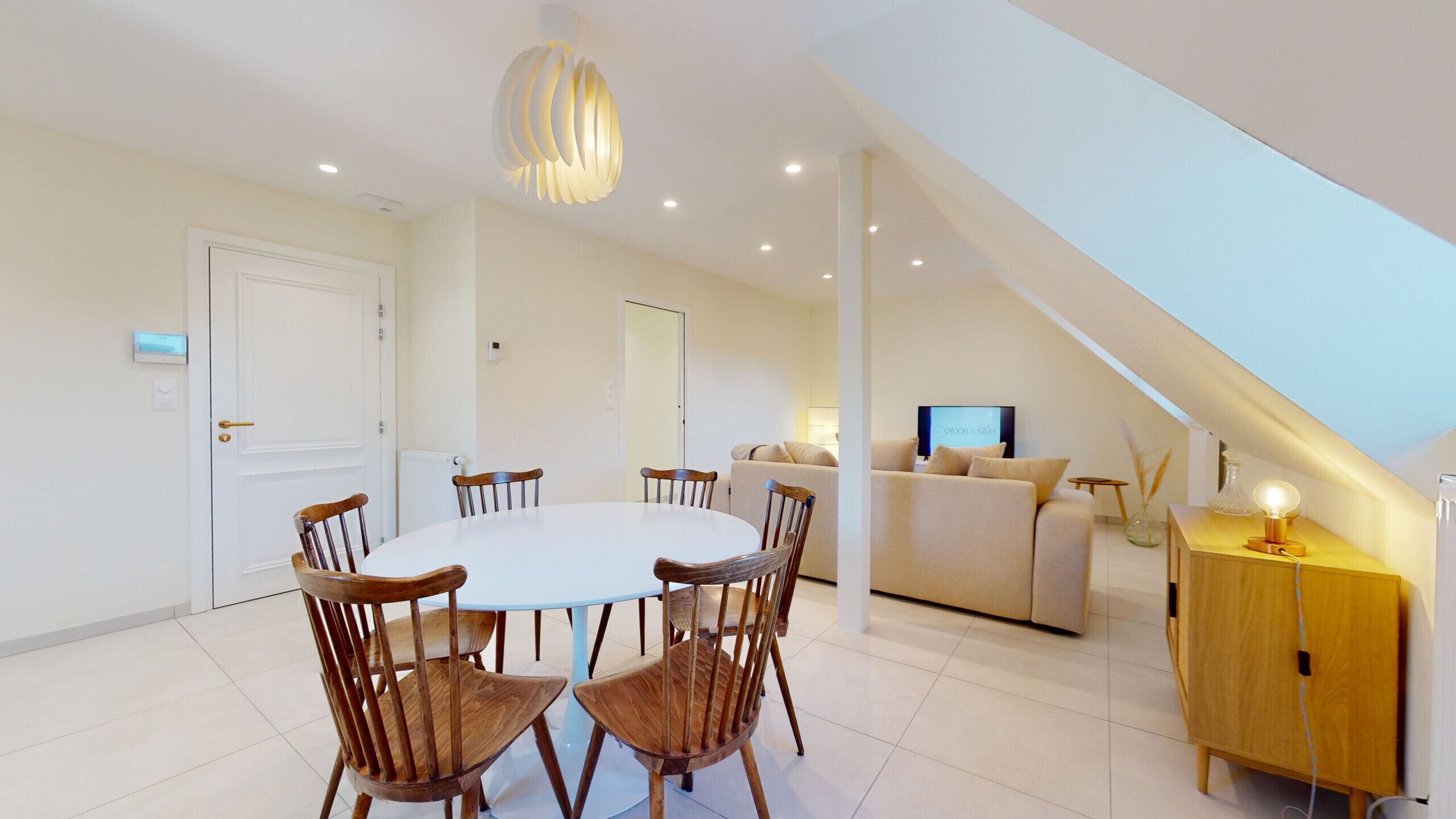Un salon moderne avec un coin repas, comprenant une table blanche, des chaises en bois, un canapé et un téléviseur.