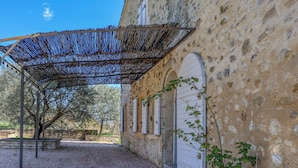 Un bâtiment doté d’une façade en pierre, d’un espace extérieur couvert avec une structure métallique et d’une porte à cadre blanc.
