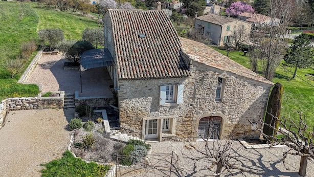 Une maison en pierre avec un toit en tuiles, une allée en gravier et un petit jardin.
