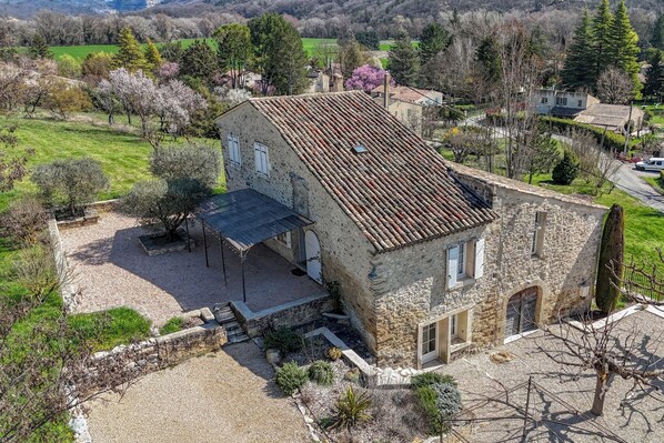 A stone building with a tiled roof, a covered patio, and a gravel driveway.