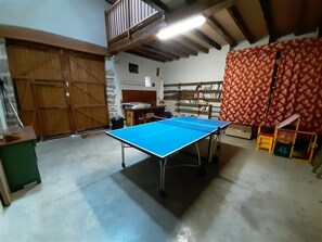 A room with a ping pong table, wooden doors, a bookshelf, and a red patterned curtain.