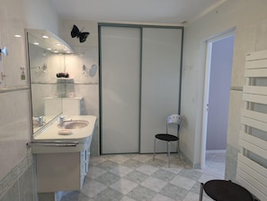 A modern bathroom with a glass shower enclosure, a white sink, and a black chair.