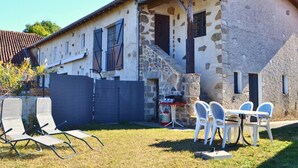 A stone house with a tiled roof, a small staircase, and a barbecue setup.