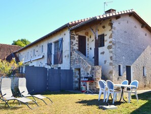 A stone house with a tiled roof, a small staircase, and a barbecue setup.