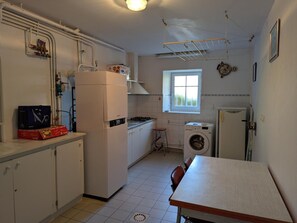 A compact kitchen with a refrigerator, washing machine, and a window providing natural light.