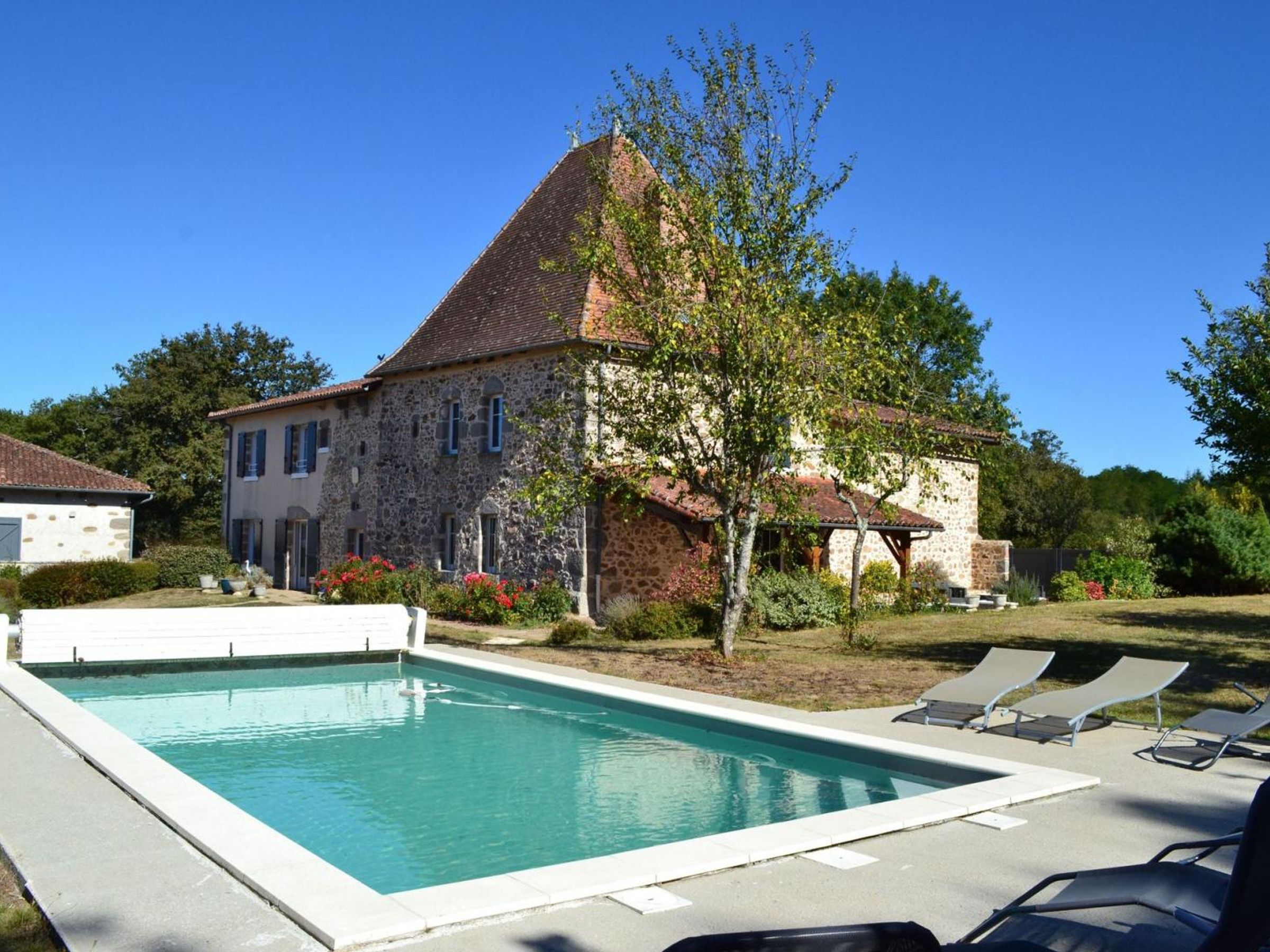 Ein Steinhaus mit Swimmingpool und Liegestühlen.
