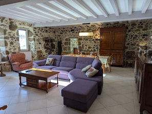 A spacious living room with a stone wall, a purple sofa, a wooden coffee table, and a dining area with a wooden table and chairs.