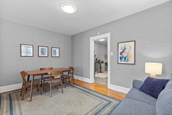 A dining area with a wooden table and chairs, a gray couch, and a lamp.