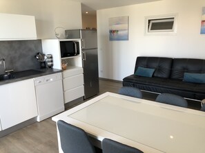 Una cocina moderna con armarios blancos, un refrigerador de acero inoxidable y un microondas. Hay una mesa de comedor con sillas, un sofá de cuero negro y una ventana con vista a la ciudad.
