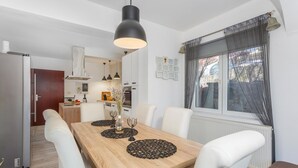 Un coin repas avec une table en bois, des chaises blanches et une suspension noire.