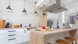 Une cuisine moderne avec des meubles blancs, un îlot central doté de tabourets, un éclairage suspendu et une hotte de cuisine en acier inoxydable.