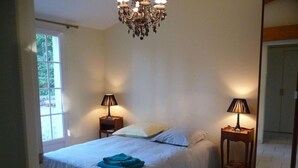 A bedroom with a bed, two bedside tables with lamps, a chandelier, and a large window. - Charming Cottage with Private Gardens, Baby Gear, Near Cognac (Cognac)
