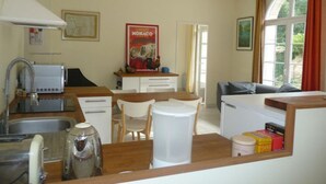 A compact kitchen with a sink, toaster, and coffee maker. There is a dining area with a table and chairs, and a living area with a sofa. A poster of Monaco is visible on the wall. - Charming Cottage with Private Gardens, Baby Gear, Near Cognac (Cognac)